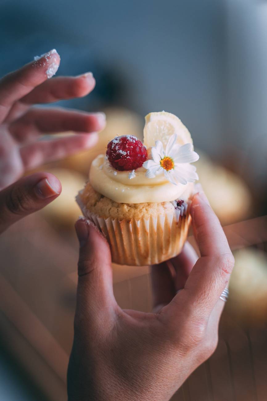 person holding cupcake with white icing
